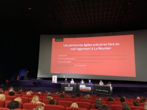 plusieurs personnes avec un micro à la main parle face à leur pupitre et à la foule, sur une scène