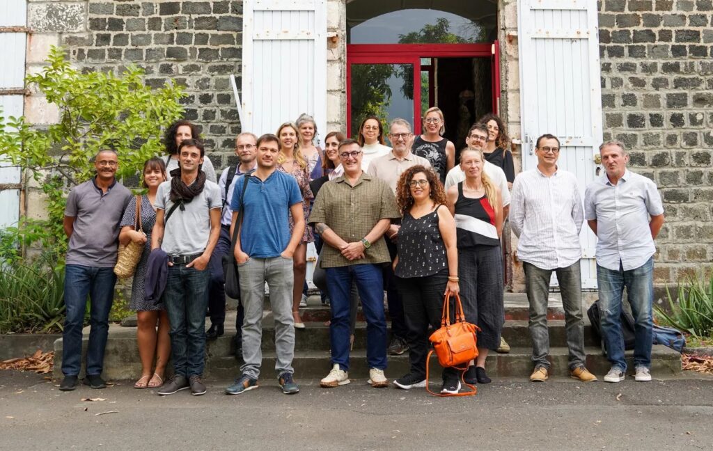 groupe de personnes représentant la premiere assemblée générale, qui posent devant un batiment.